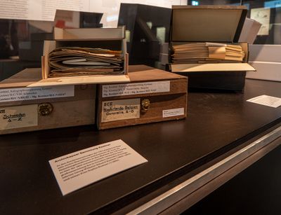 Mehrere beschriftete Archivkapseln der Universitätsbibliothek liegen in einer Ausstellungsvitrine
